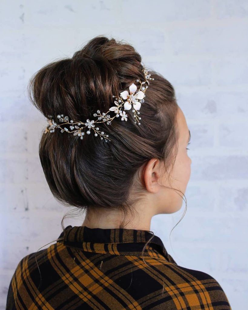 Hairstyle for women: back of the head of a dark-haired woman with a bun and a flower hairband. 