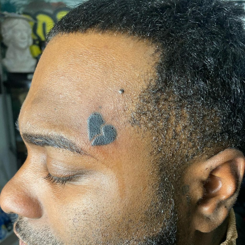 Schwarzes Tattoo mit gebrochenem Herzen auf der Stirn