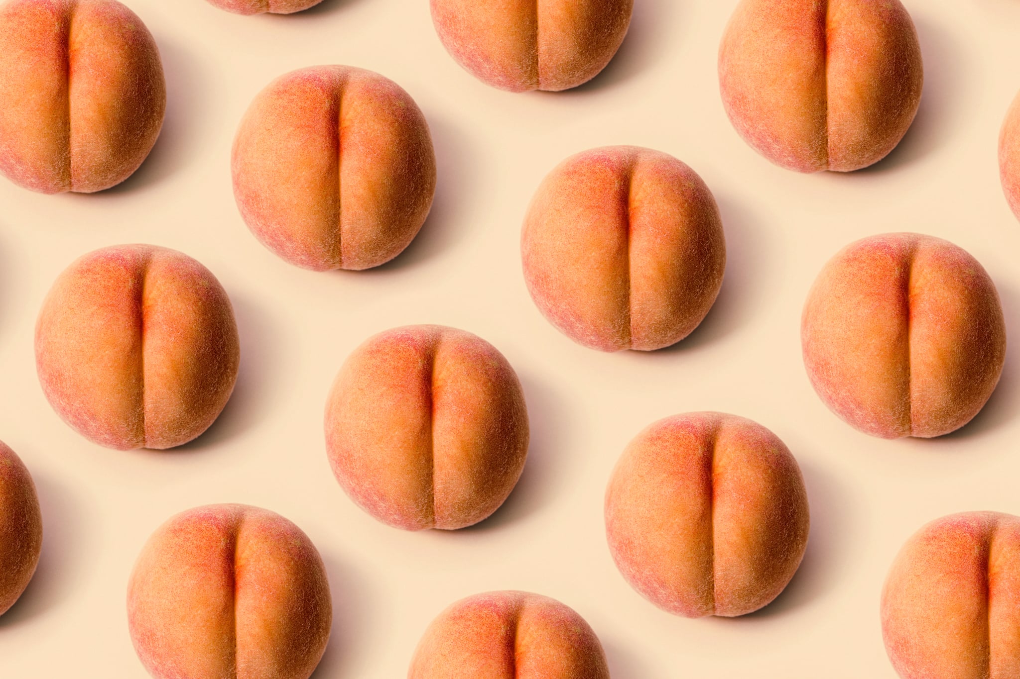 A detailed image of a freshly picked ripe peach.  Photographed on a peach colored background.