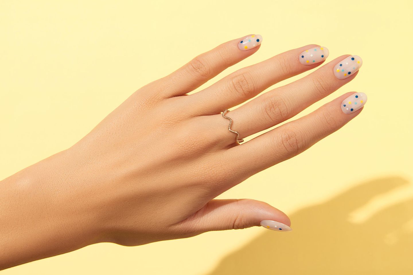 Nail trends 2022: hand with dotted nails on yellow background